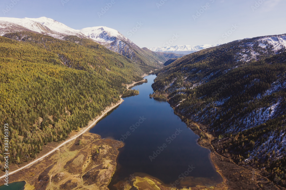 Colourful mountains valley, blue snow covered peaks, orange and green autumn forest and mountain lake. Aerial view