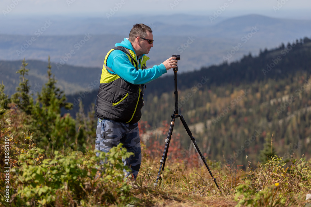 a photographer shoots an autumn landscape with a small camera on a tripod. side view of the process of taking photos from a tripod with a man in the frame
