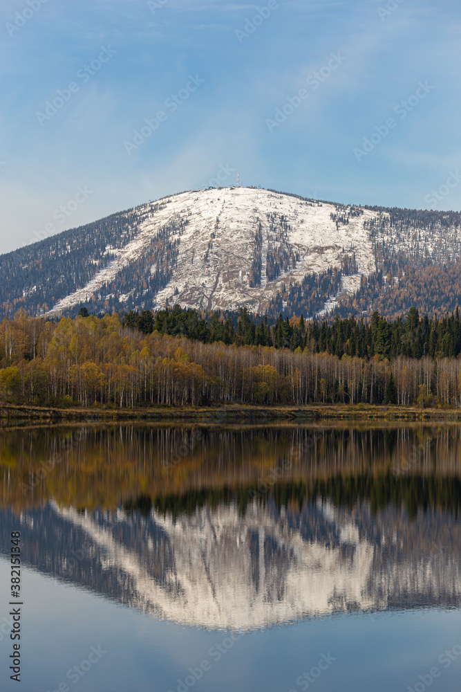 view of the ski resort in autumn. a mountain range covered with snow with ski slopes is reflected in the surface of a large lake