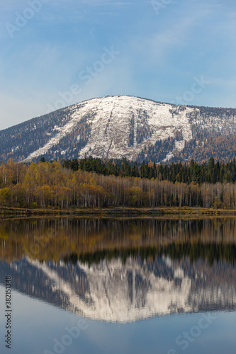 view of the ski resort in autumn. a mountain range covered with snow with ski slopes is reflected in the surface of a large lake
