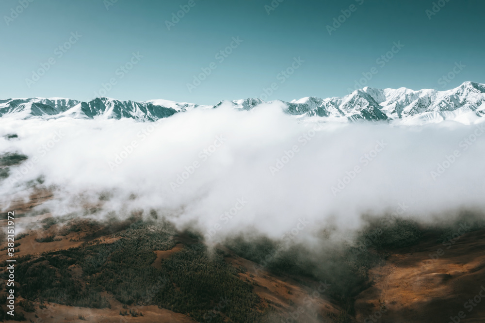 Aerial drone view above clouds on mountains landscape  with snow peaks and fur forests