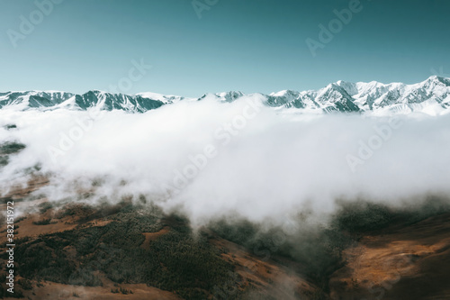 Aerial drone view above clouds on mountains landscape with snow peaks and fur forests