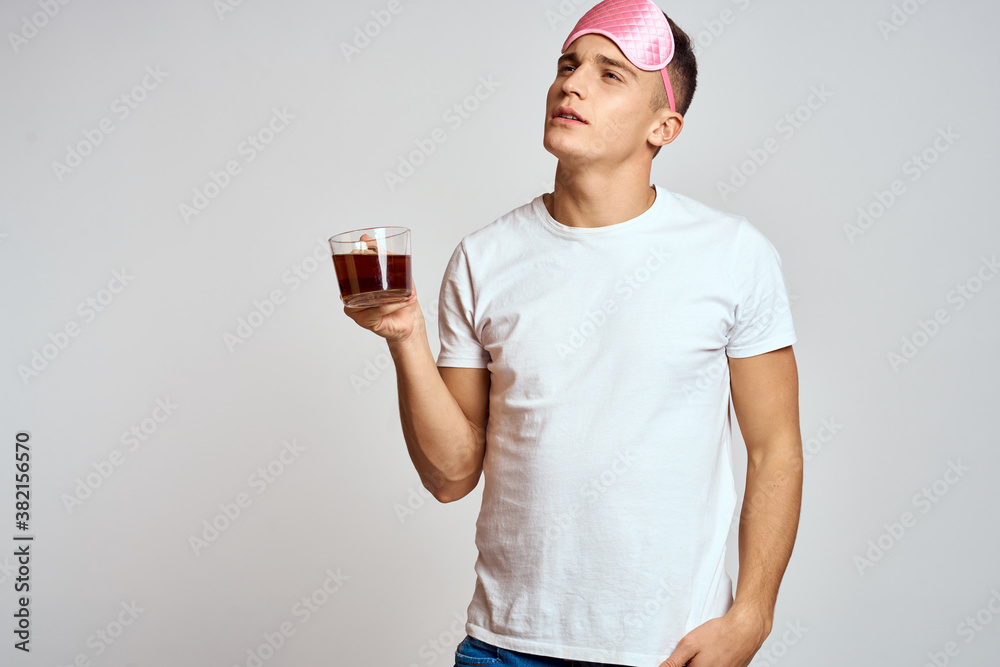 handsome man with pink sleep mask and with a cup of tea in hand pulls himself up on a light background handsome man with pink sleep mask and with a cup of tea in hand pulls himself up on a light background