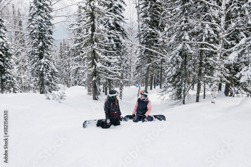 snowboarders female seating and rest in winter snow-covered spruce forest, fresh snow powder, freeride on  sunny winter day, Woman snowboarding