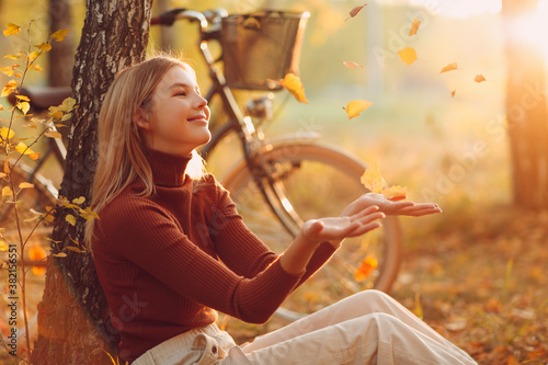 Happy active young woman sitting with vintage bicycle in autumn park at sunset