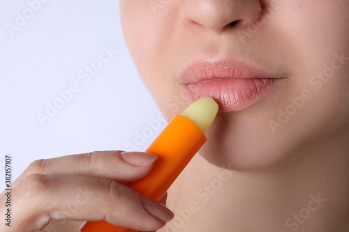 Woman applying hygienic lipstick on lips against white background, closeup