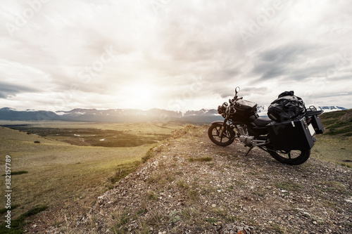 Motorcycle with trunks and bags on a long journey standing on the cliff in mountains landscape. Altai mountain