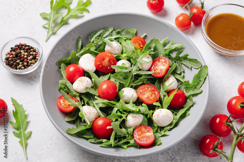 Diet and healthy salad with arugula, cherry tomatoes, mozzarella cheese and salad dressing on white background