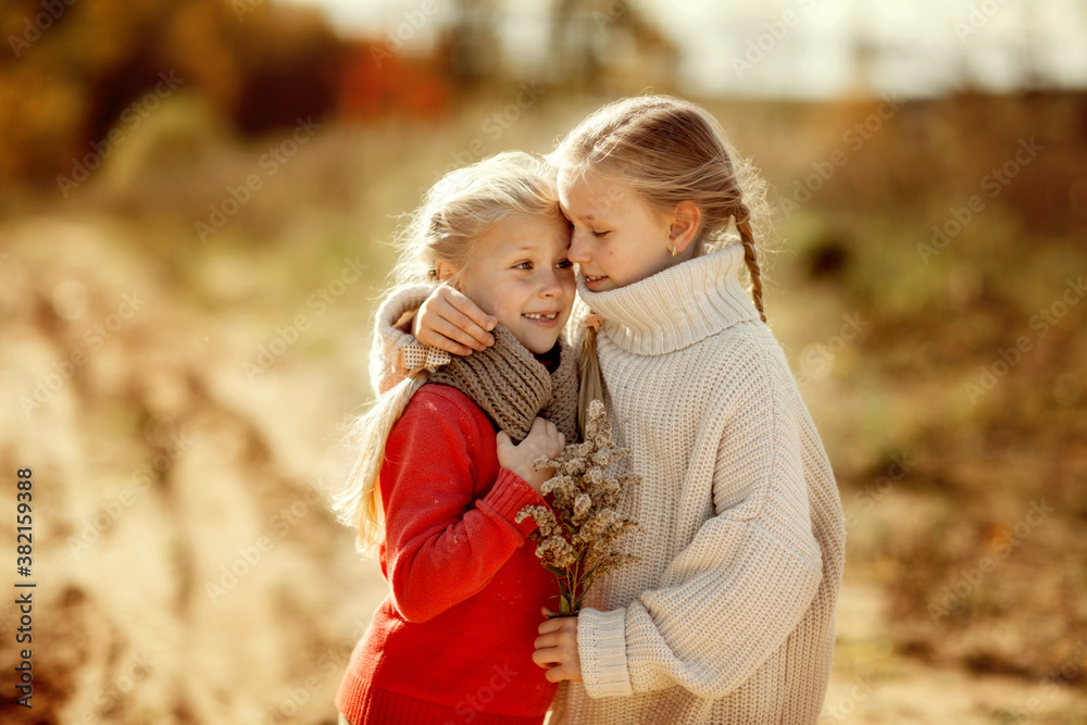 Two sisters in warm sweaters hug and run along the trail in the autumn forest. Two sisters in warm sweaters hug and run along the trail in the autumn forest.