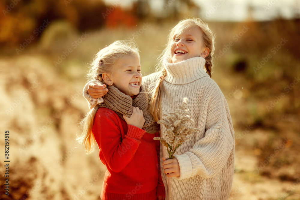 Two funny sisters in warm sweaters hug and run along the trail in the autumn forest.