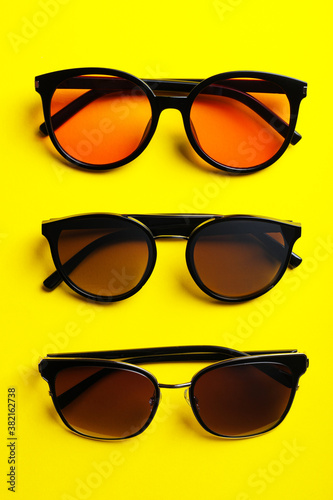 Many stylish sunglasses on yellow background, flat lay