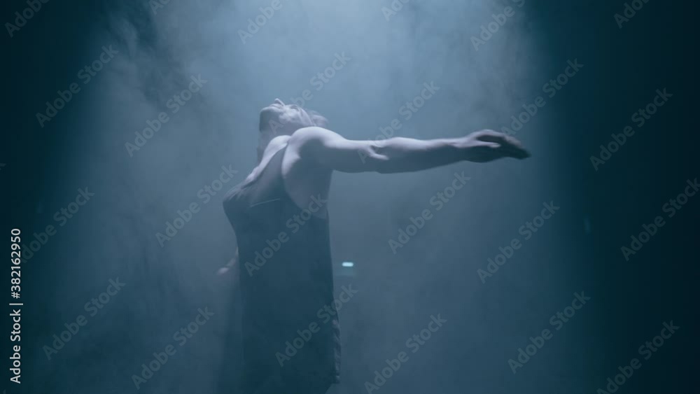Young attractive man dancer is spinning around on dark smoke background Young attractive man dancer is spinning around on dark smoke background