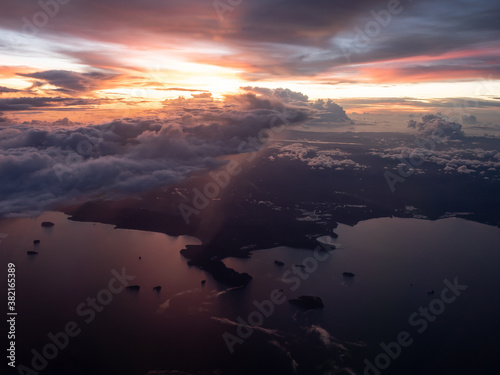 aerial view of sunset from aircraft window seat. broken cloud overcast the terrain. flying along the coast. rain precipitation from cloud falling into earth.