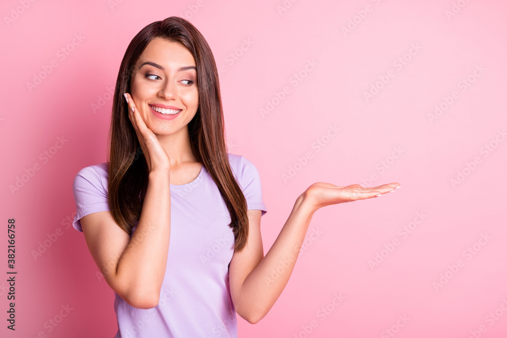Photo portrait of nice curious girl looking at blank space on palm smiling isolated on pastel pink color background Photo portrait of nice curious girl looking at blank space on palm smiling isolated on pastel pink color background