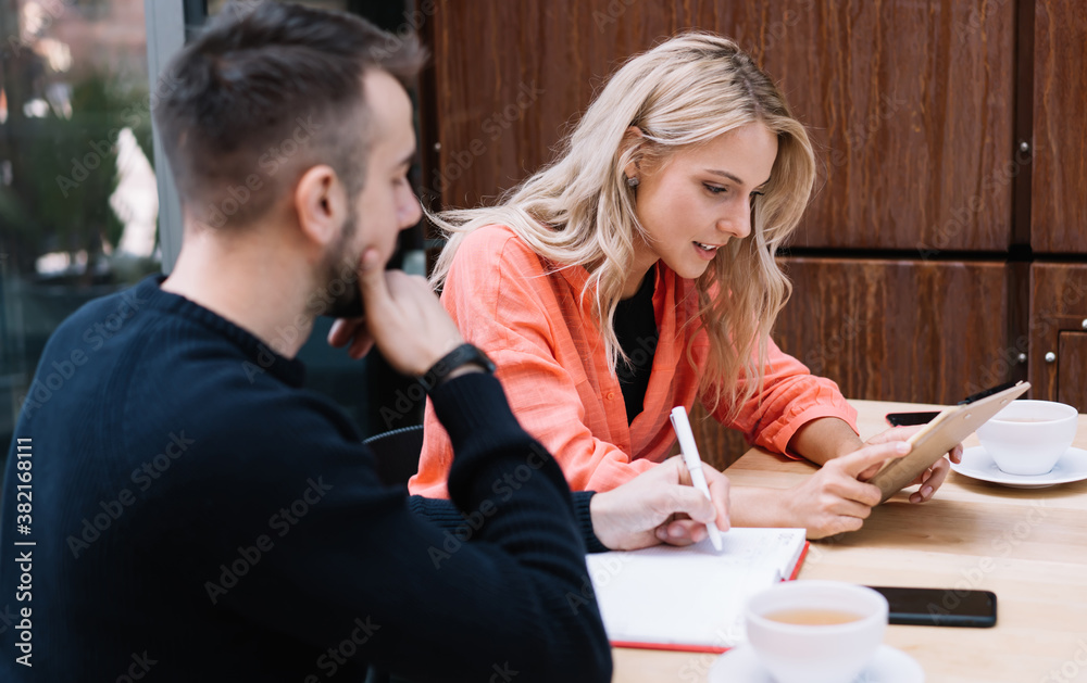 Serious male and female friends discussing common project together reading information from planer, young woman employee having positive conversation with man colleagues share ideas in cafe Serious male and female friends discussing common project together reading information from planer, young woman employee having positive conversation with man colleagues share ideas in cafe
