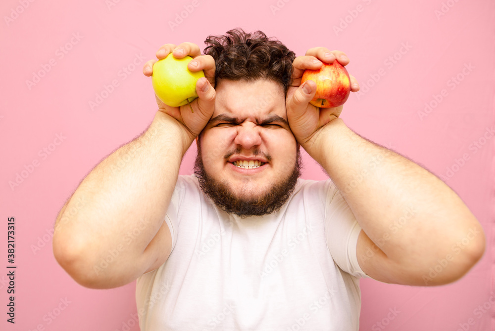 Close up portrait of emotional fat guy with apples in his hands, looking  dissatisfied into the camera and yelling. Hungry fat man with apples in  hands isolated on pink background. Stock Photo |