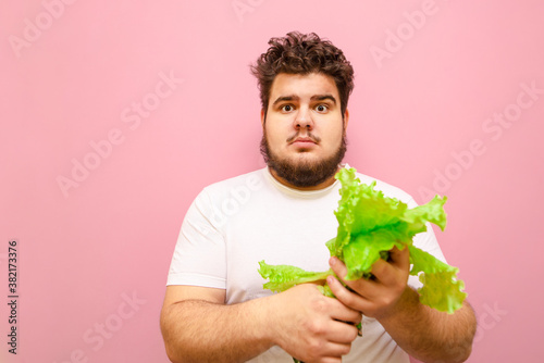 Photos Surprised fat man isolated on pink background with lettuce in his hands, looks into camera with shocked face
