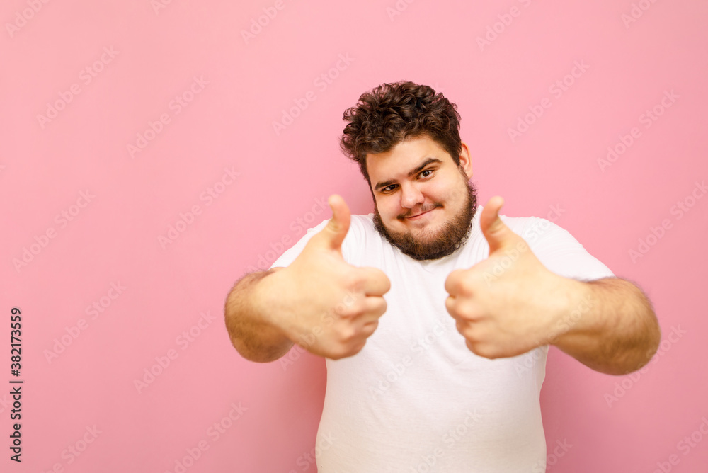 Cheerful bearded fat man in white tshirt isolated on pink background, looks into camera and