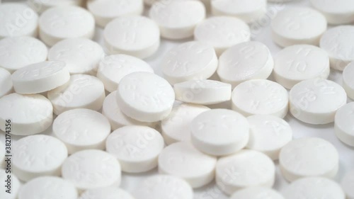 Slow rotation of a large group of white pills on a white background and one yellow pill on the middle. A medicine concept. Close up shot with selective focus