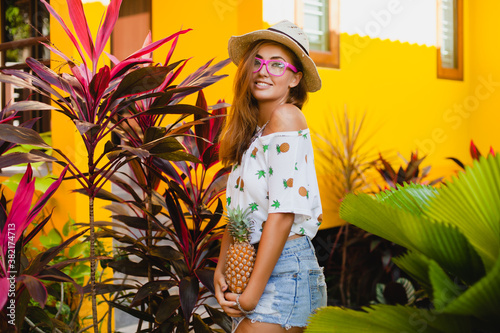 attractive smiling woman on vacation in printed t-shirt straw hat summer fashion, hands holding pineapple
