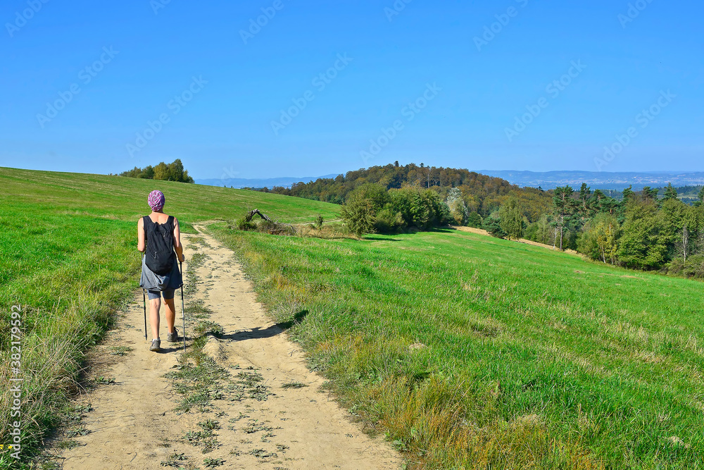 Backpacker woman hiking on the country road. Beautiful nature around them. Outdoor activity and walking in the countryside.