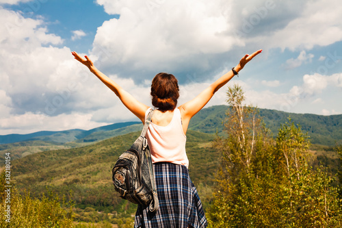 Happy young woman holding her hands up and enjoying beautiful mountain landscape. Back view. Freedom concept. Vacation in the mountains.