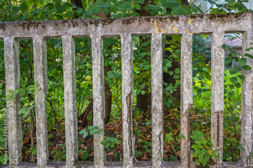 Old lattice concrete broken fence close up, in the background green leaves of trees, horizontal orientation Old lattice concrete broken fence close up, in the background green leaves of trees, horizontal orientation