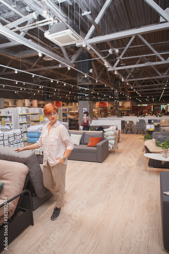 Vertical shot of a young woman walking at furniture store, examining couches on sale, copy space