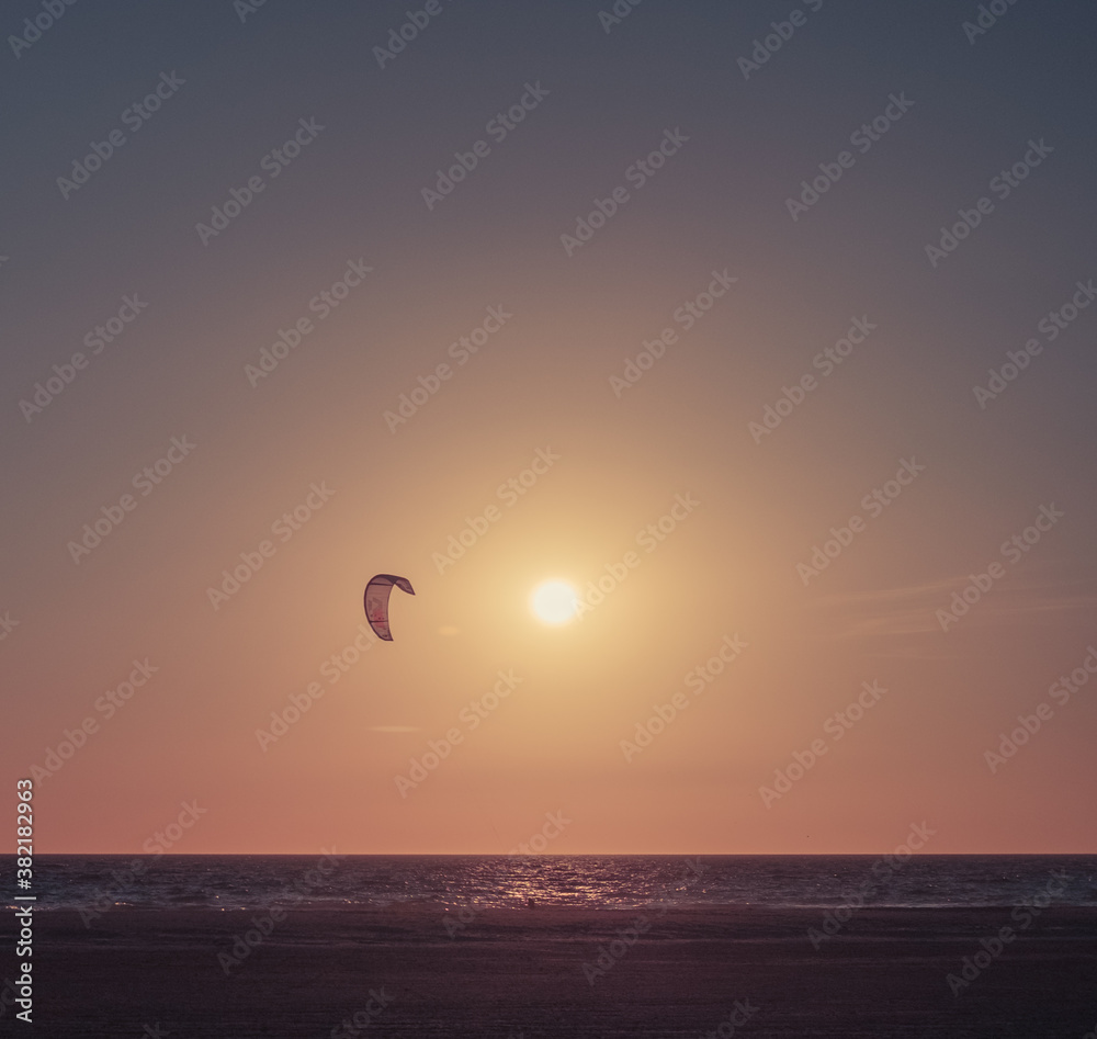 Beautiful september sunset with a kitesurfer fliying. Golden hour. By the sea. Beach landscape. 