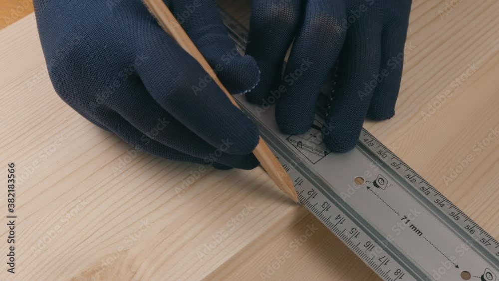 a builder draws a ruler with a pencil on a pine wood board
