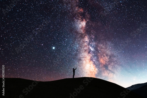 Beautiful starry sky with bright milky way galaxy. Night landscape . Person silhouette stands on the hill and looking at the starry sky.