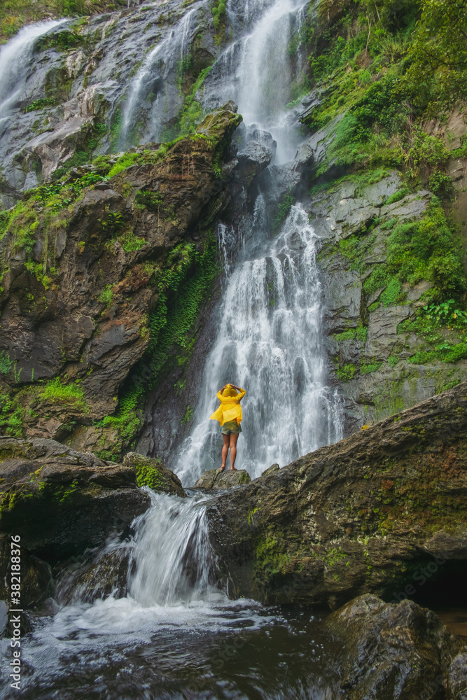 Obraz premium Woman standing on a rock with a waterfall in front