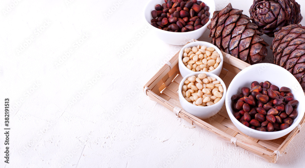 Shelled and unshelled pine nuts and pine cones on the white table. Copy space Shelled and unshelled pine nuts and pine cones on the white table. Copy space