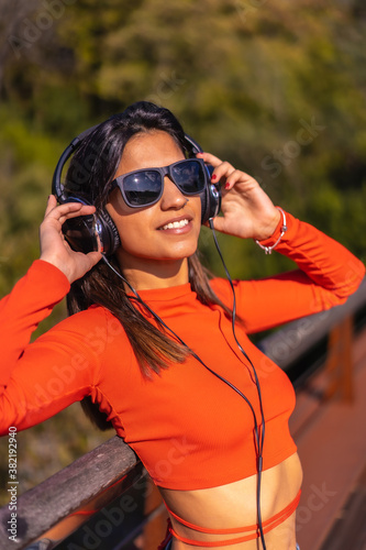 Lifestyle, brunette Caucasian girl enjoying music with headphones in a park. Young girl in red t-shirt and jeans