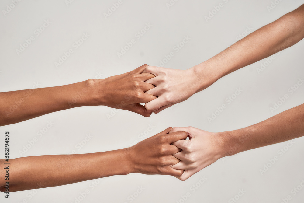 Close up of female hands holding together with fingers crossed isolated over grey background. Diversity, support, friendship concept