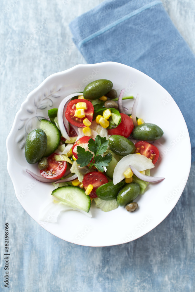Healthy Salad with Green Olives, Baby Spinach, Cucumber, Cherry Tomatoes and Capers. Bright wooden background. Top view. Close up.