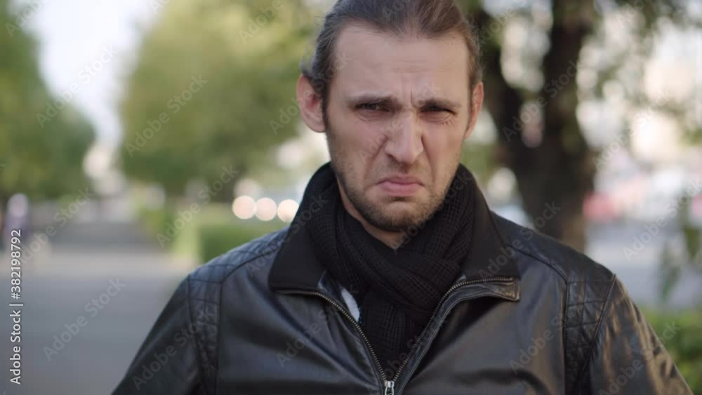 Young man in black jacket expressing disgust and disapproval with negative facial expressions outdoors. Facial expression. Young man in black jacket expressing disgust and disapproval with negative facial expressions outdoors. Facial expression.