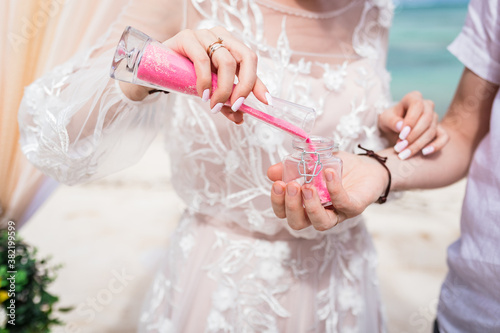 Close up view of bride and groom filling color sand into the jar at the wedding sand ceremony on the paradise beach, Punta Cana, Dominican Republic