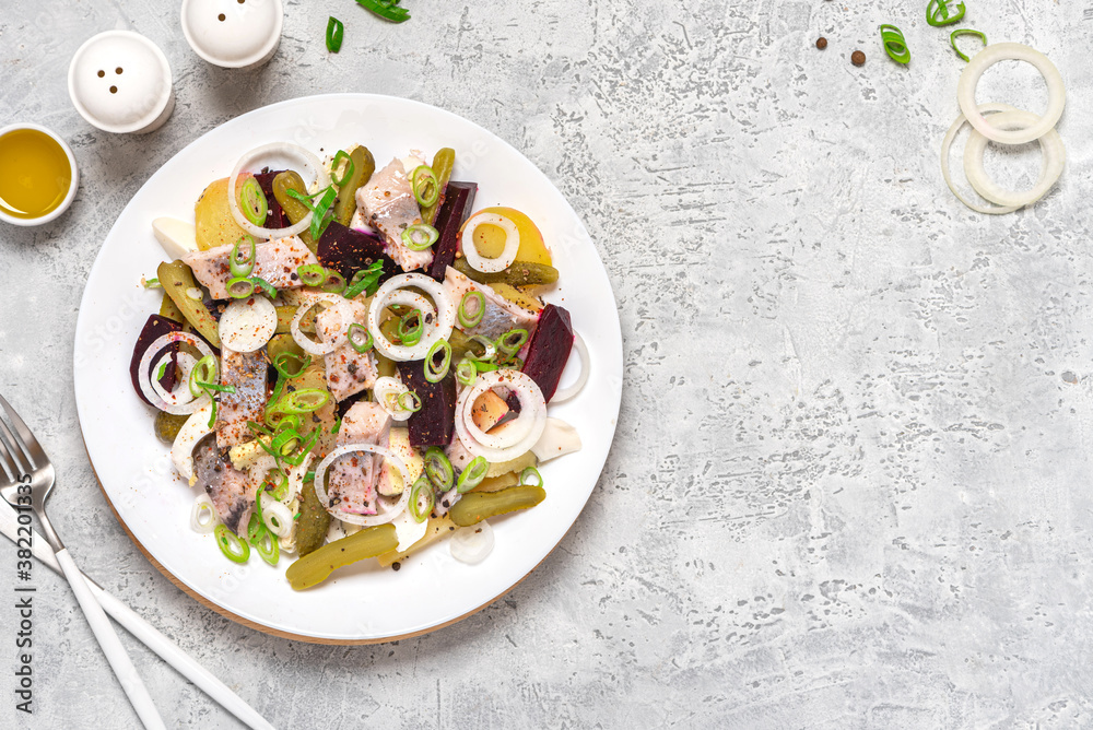 Salad of herring, beets, potatoes, eggs, pickling cucumbers and spices in white plate on gray concrete background top view. Free space for text