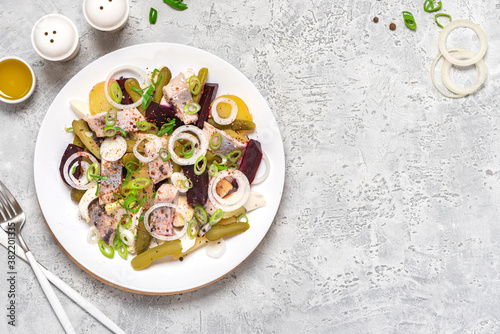 Salad of herring, beets, potatoes, eggs, pickling cucumbers and spices in white plate on gray concrete background top view. Free space for text