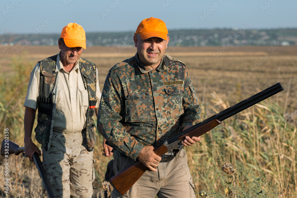 Duck hunters with shotgun walking through a meadow. Duck hunters with shotgun walking through a meadow.