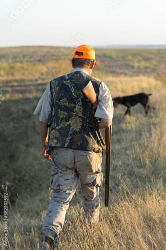 Duck hunter with shotgun walking through a meadow. .Rear view of a man with a weapon in his hands.