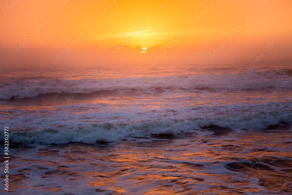 Early morning sunrise on the beach at St Augustine, Florida with waves and the sun reflected in the surf, making an orange surf.