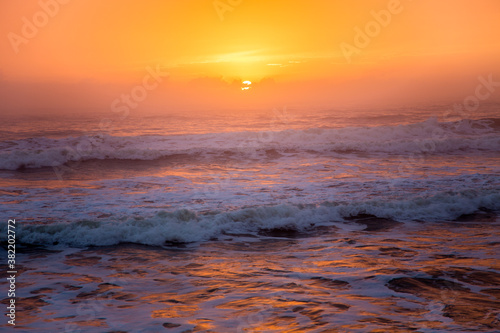 Early morning sunrise on the beach at St Augustine  Florida with waves and the sun reflected in the surf  making an orange surf.