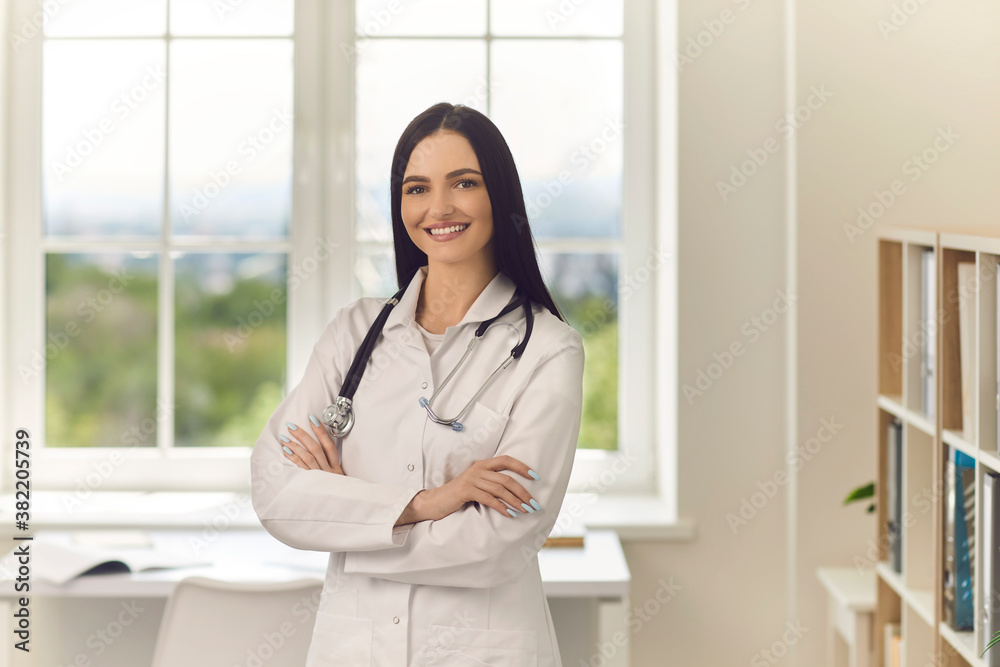 Young doctor standing arms crossed looking at camera and smiling in modern hospital office Young doctor standing arms crossed looking at camera and smiling in modern hospital office