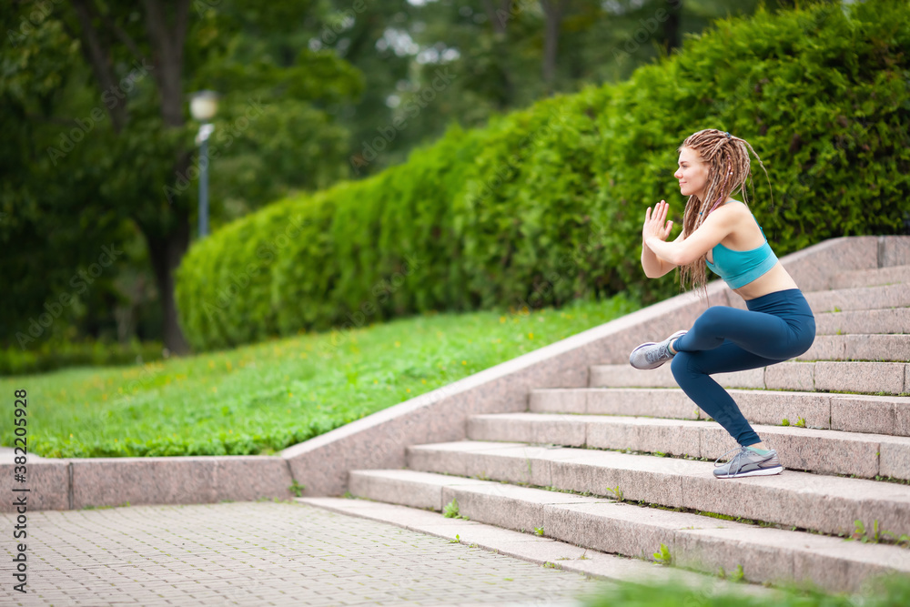 .Young woman with dreadlocks balancing on one leg. Sits in a difficult pose from yoga on the stairs in the park.