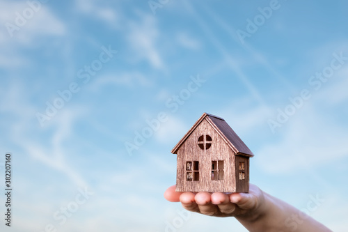 The house in human hands on the blue sky with clouds