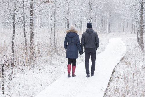 Fotografía Young adult couple holding each other hands and walking on white snowy boardwalk