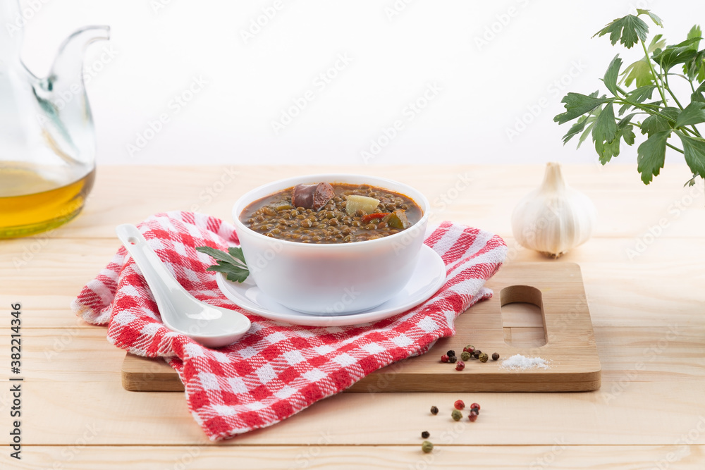 Traditional Spanish dish of lentil stew with chorizo and potatoes, on a light wooden base.