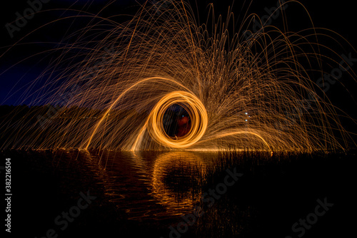 Burning Steel Wool spinning, Trajectories of burning sparks on the surface of water lake at the background of spring night landscape